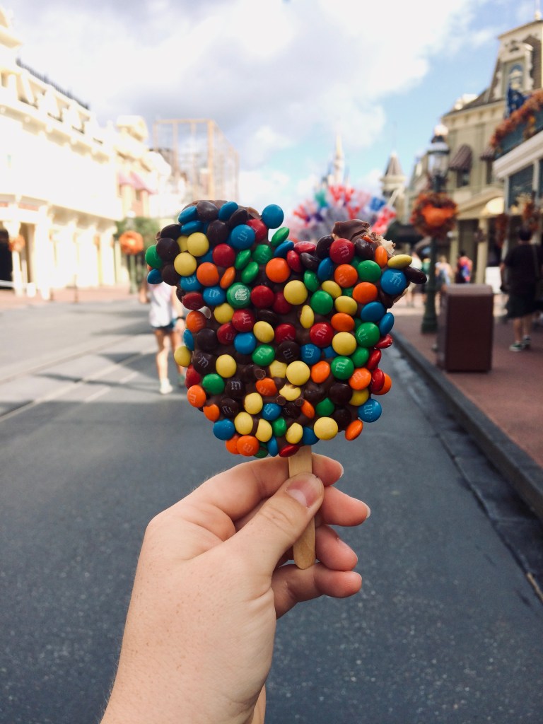 Hand holding Mickey shaped rice crispy treat with m&ms on Main Street at Magic Kingdom, Walt Disney World