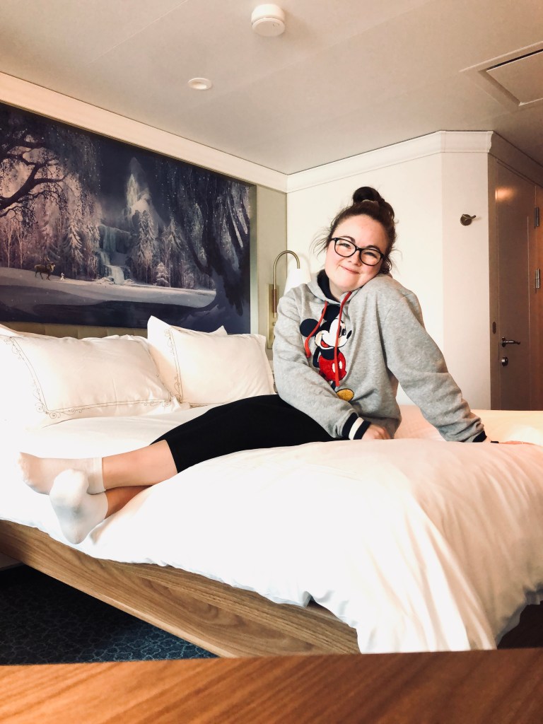 Girl with mickey sweater sitting on a bed in a stateroom onboard the Disney Wish