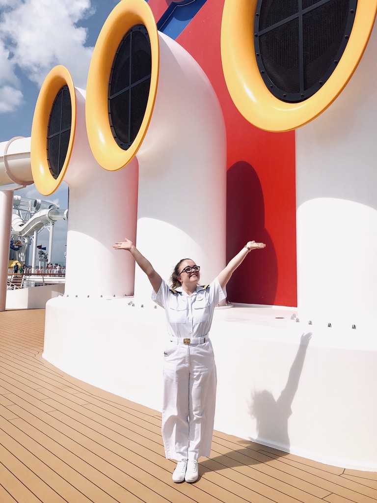 Disney Cruise Line Crew Member dressed in Officer whites posing in front of Mickey Funnels on a cruise ship
