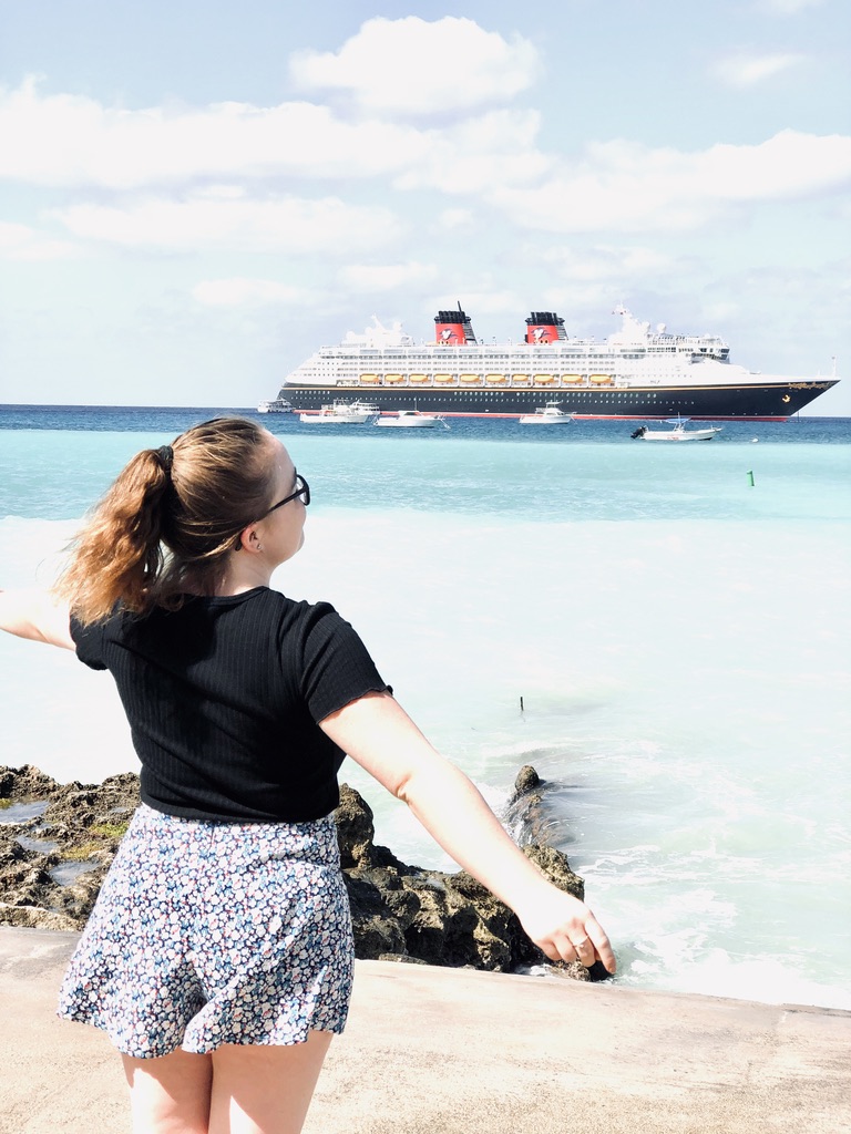Disney Cruise Line Crew Member posing in front of Disney Magic cruise ship at Cayman Islands