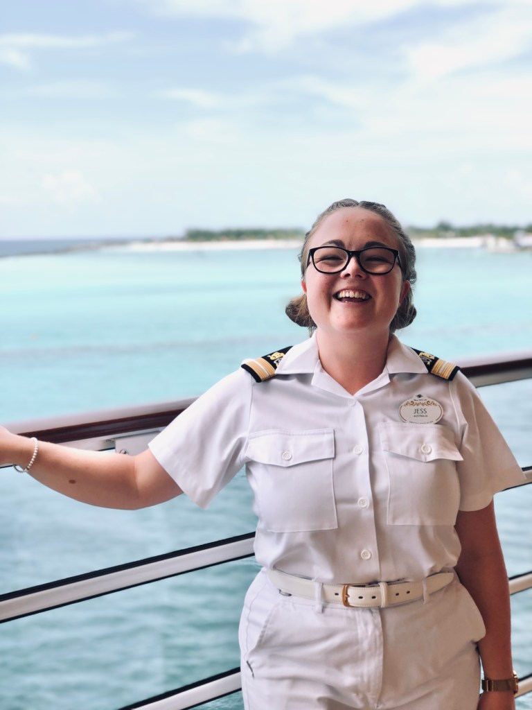Disney Cruise Line officer smiling on deck with Castaway Cay in the background