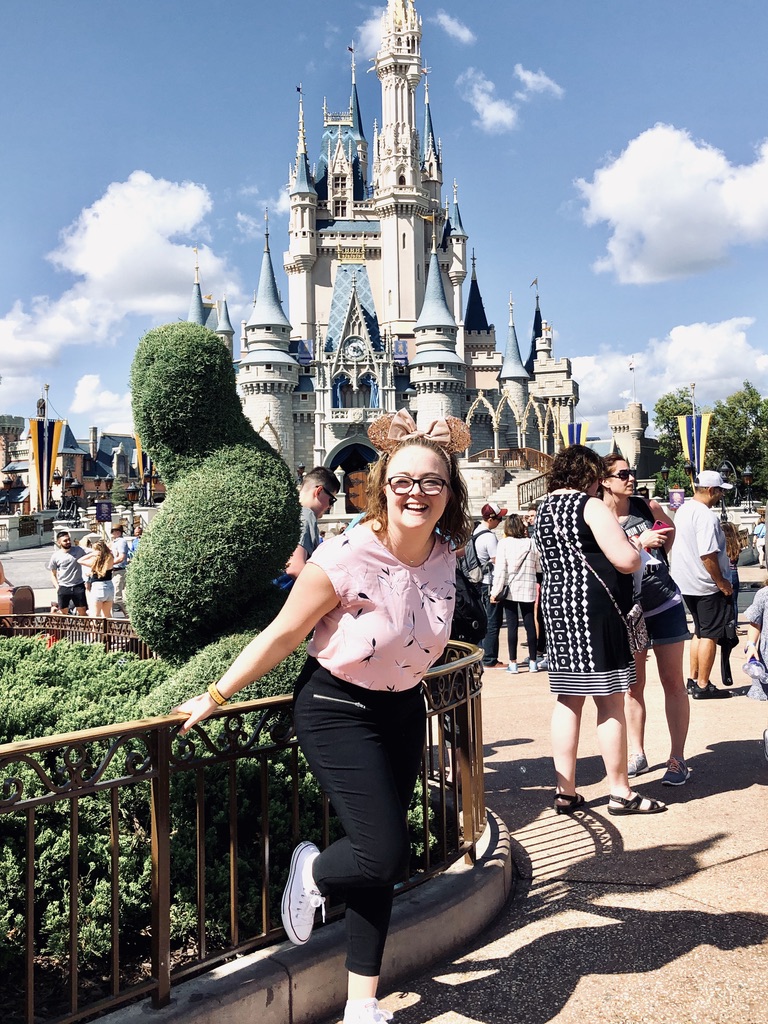 Disney crew member smiling in front of Cinderella castle on a sunny day