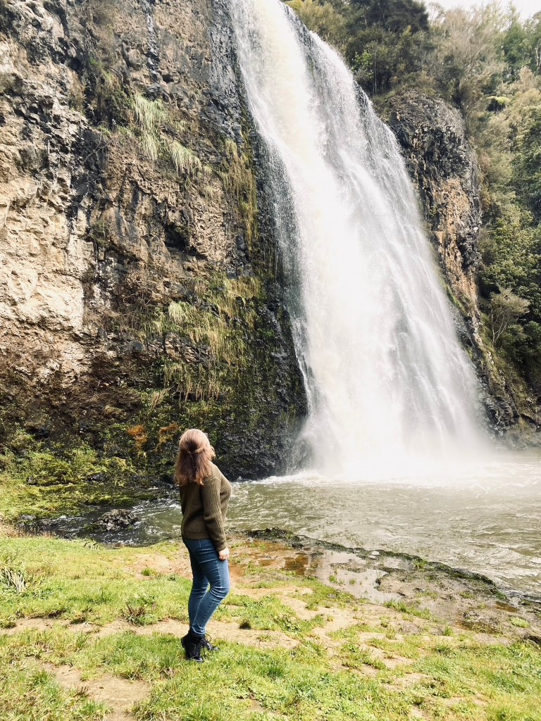 Girl in green sweater looking up at waterfall in New Zealand
