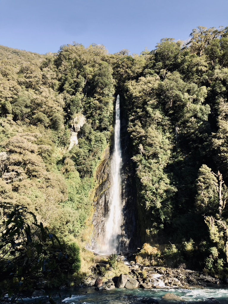Tall waterfall with green trees surrounding on a road trip on New Zealand's South Island
