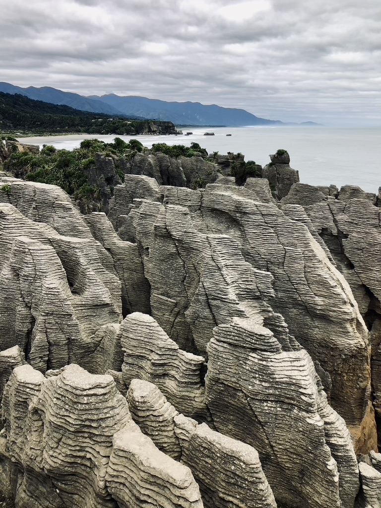 Unusual rock formations with ocean and mountains in the distance at Pancake Rocks in New Zealand