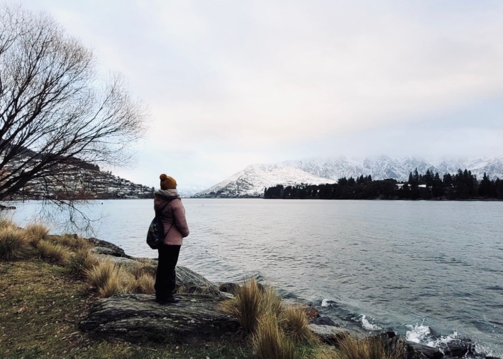 Girl looking out at lake and snow capped mountains in winter in Queenstown, New Zealand
