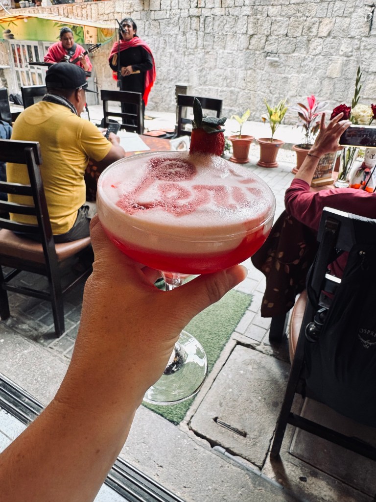 Hand holding strawberry flavored Pisco sour with "Peru" stamped on to froth in Aguas Calientes, Peru