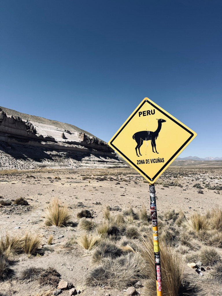 Yellow tourist warning sign featuring vecuna icon and Peru with desert in background on the way to Colca Canyon, Peru