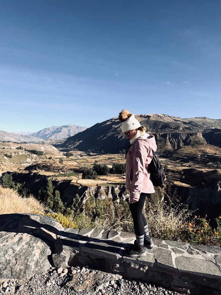 Girl in pink jacket walking with Colca Canyon in background, Peru