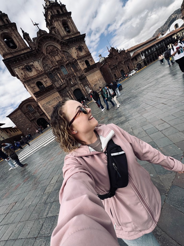 Girl in pink jacket taking selfie while walking around Plaza de Armas in Cusco, Peru