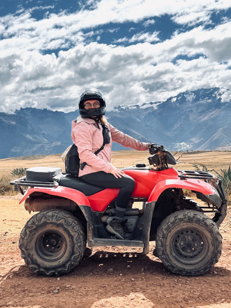Girl in pink coat sitting on ATV with Andes mountains in the background in Peru