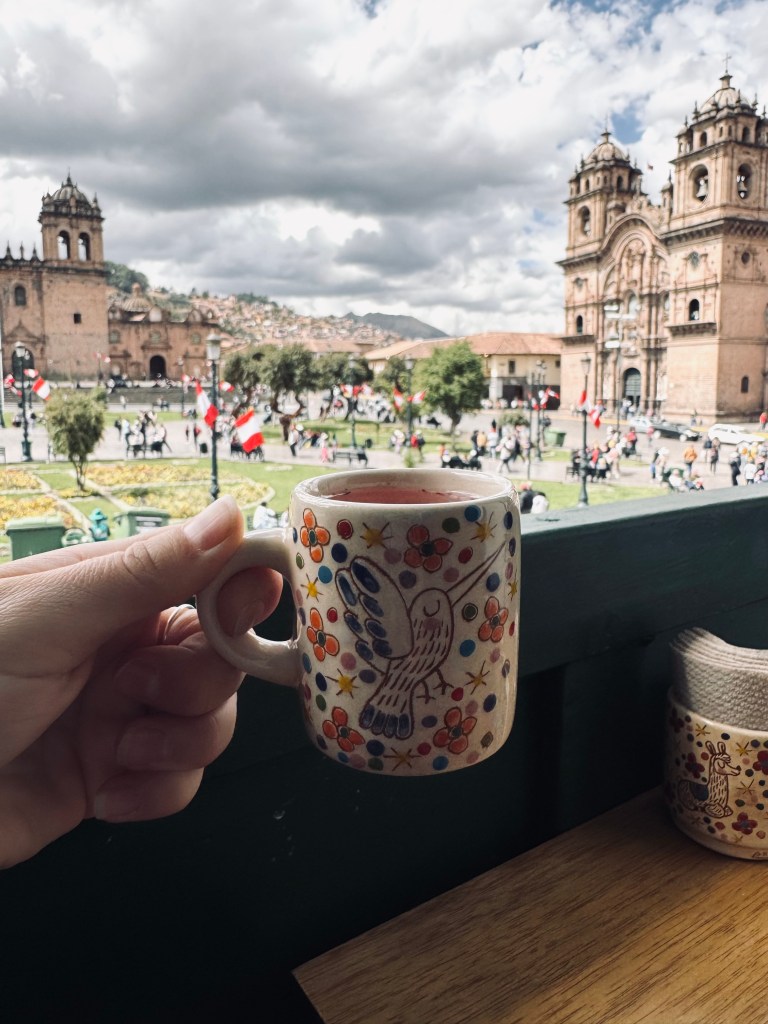 Hand holding cute cup of tea on balcony with Plaza de Armas in background in Cusco, Peru
