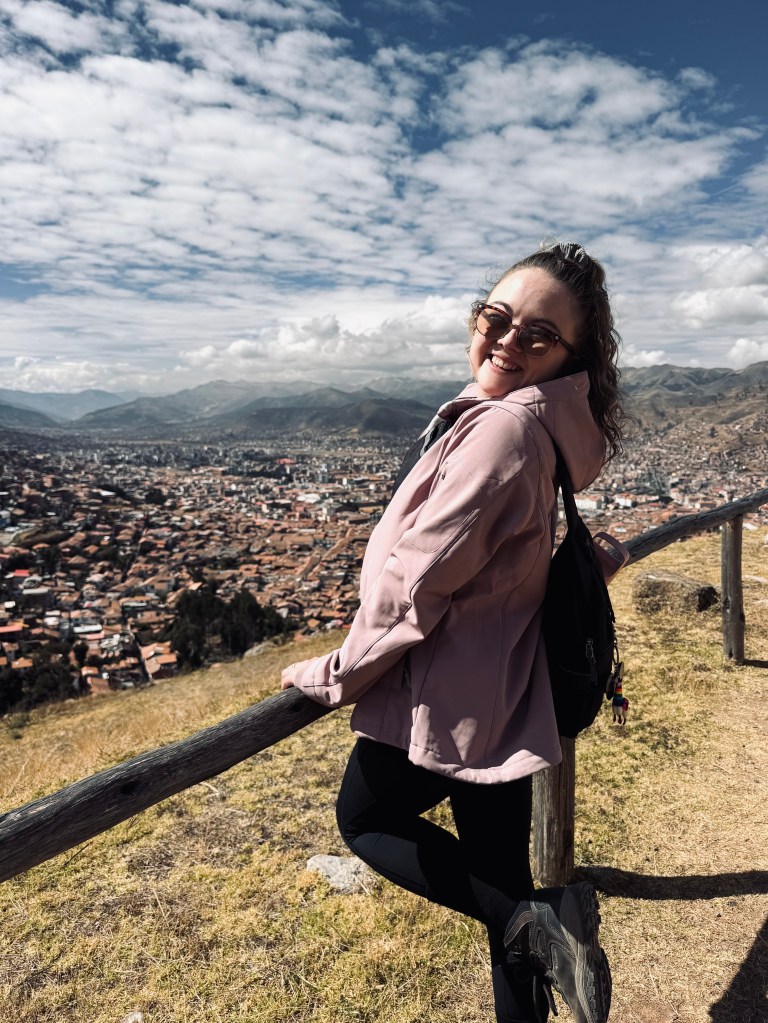 Girl in pink jacket holding railing with view of Cusco city in background in Peru