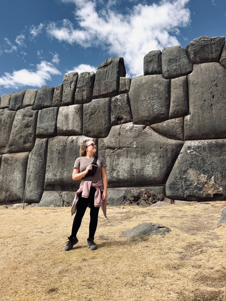 Girl in pink jacket standing in front of ruins at sacsayhuamán in Cusco, Peru