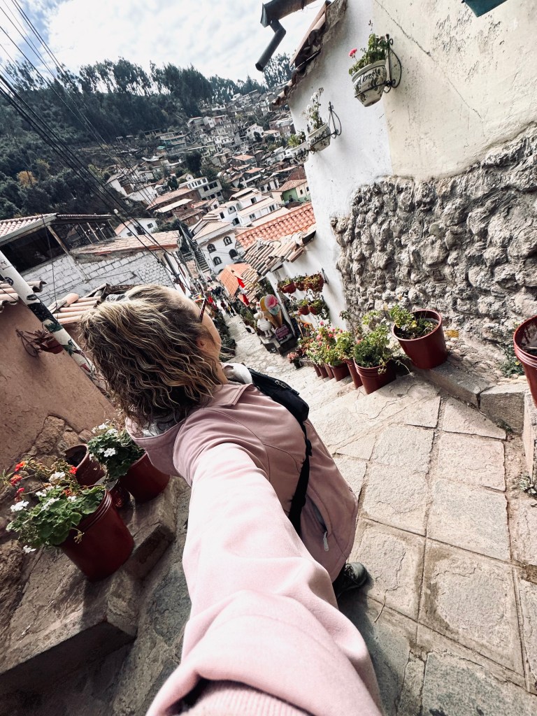 Girl in pink jacket taking selfie looking back at Cusco views in the San Blas neighbourhood, Peru