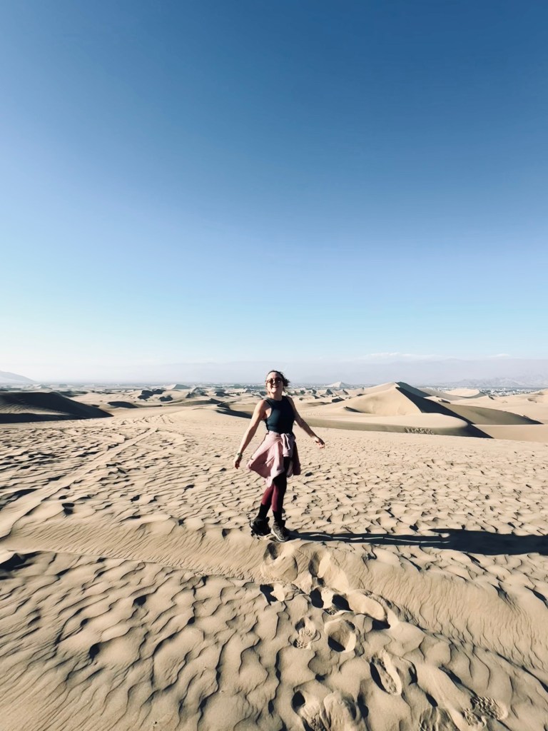 Girl walking on sand in the middle of the desert with sand dunes in background in Huacachina, Peru