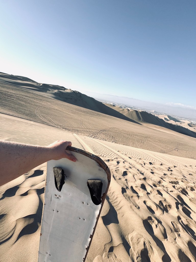 Hand holding sandboard with sand dunes in background in Huacachina, Peru