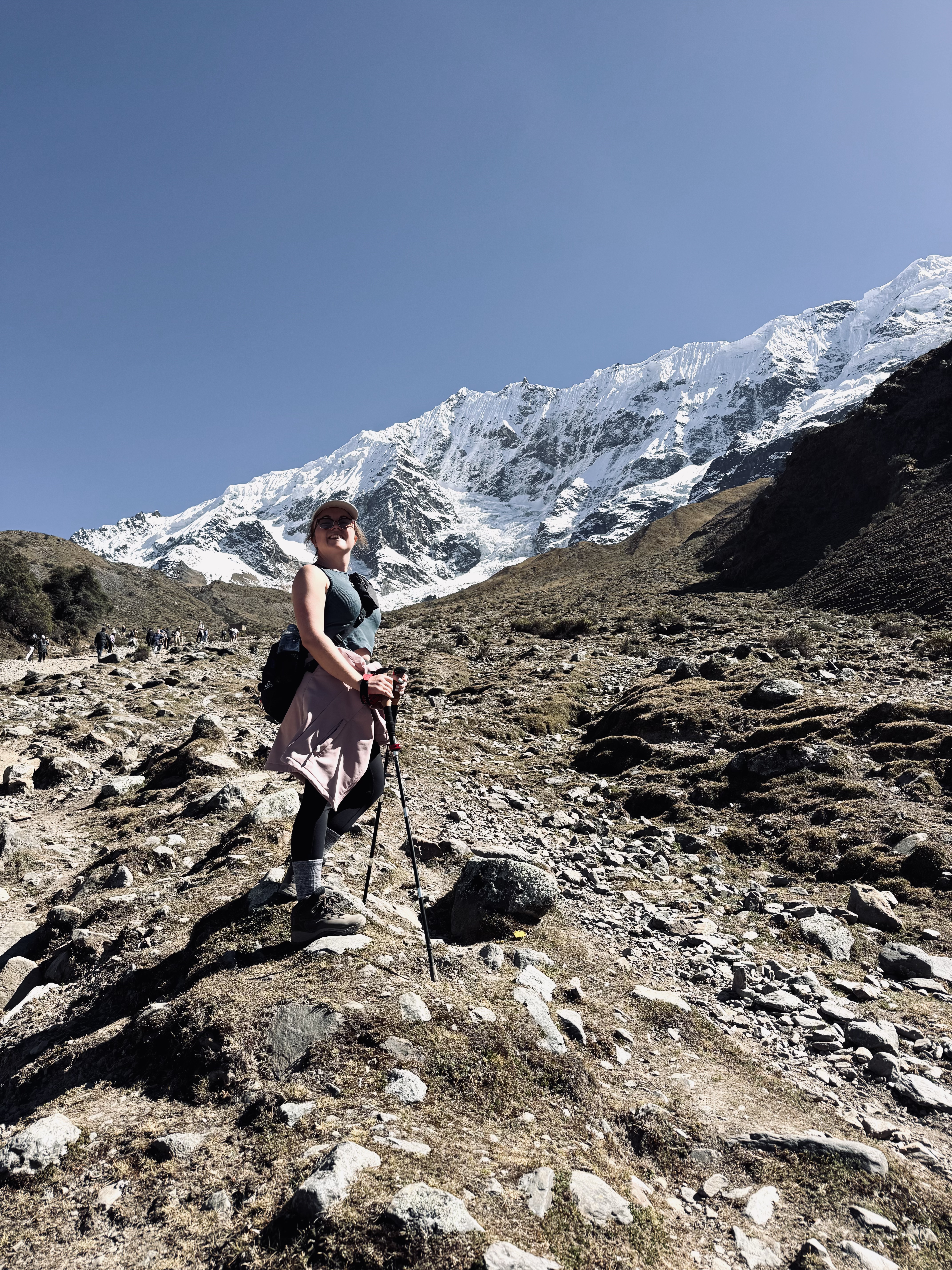 Girl with hiking poles looking back with snow covered mountains in background at Humantay Lake, Peru