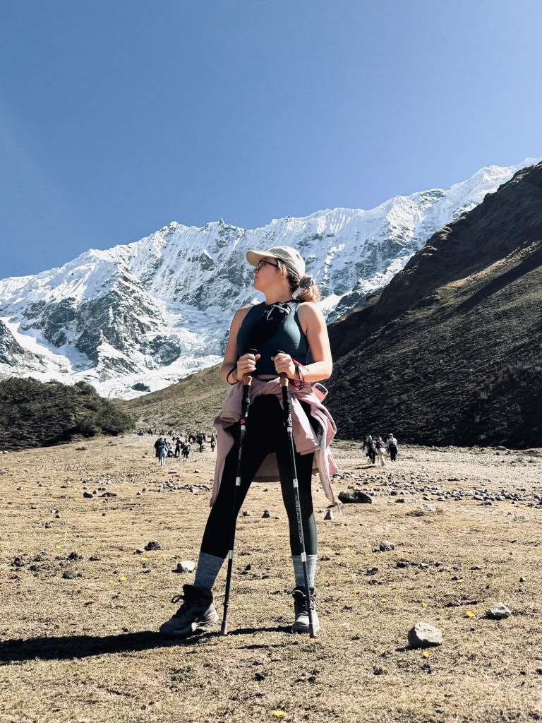Girl holding trekking poles looking to the side with snow covered mountains in background on trek to Humantay Lake, Peru