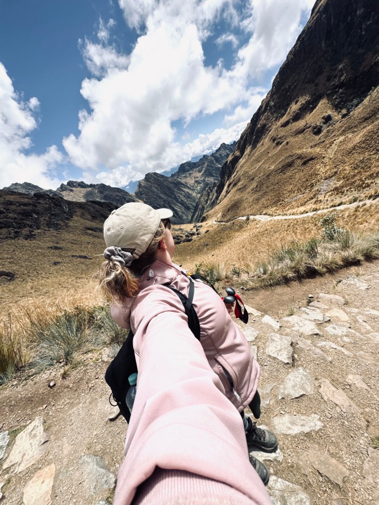 Girl taking selfie at the top of dead womans pass with mountains in the background on the Inca Trail in Peru