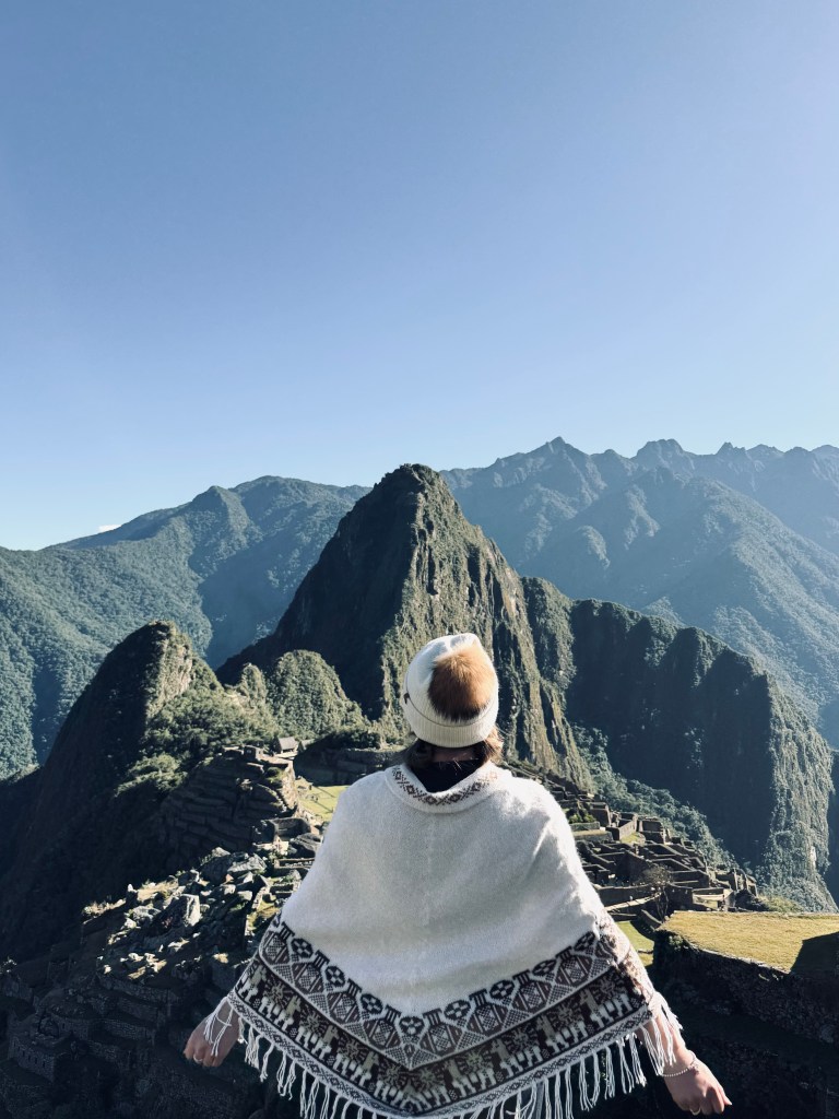 Girl wearing poncho looking at Machu Picchu on a sunny day on the Inca Trail in Peru