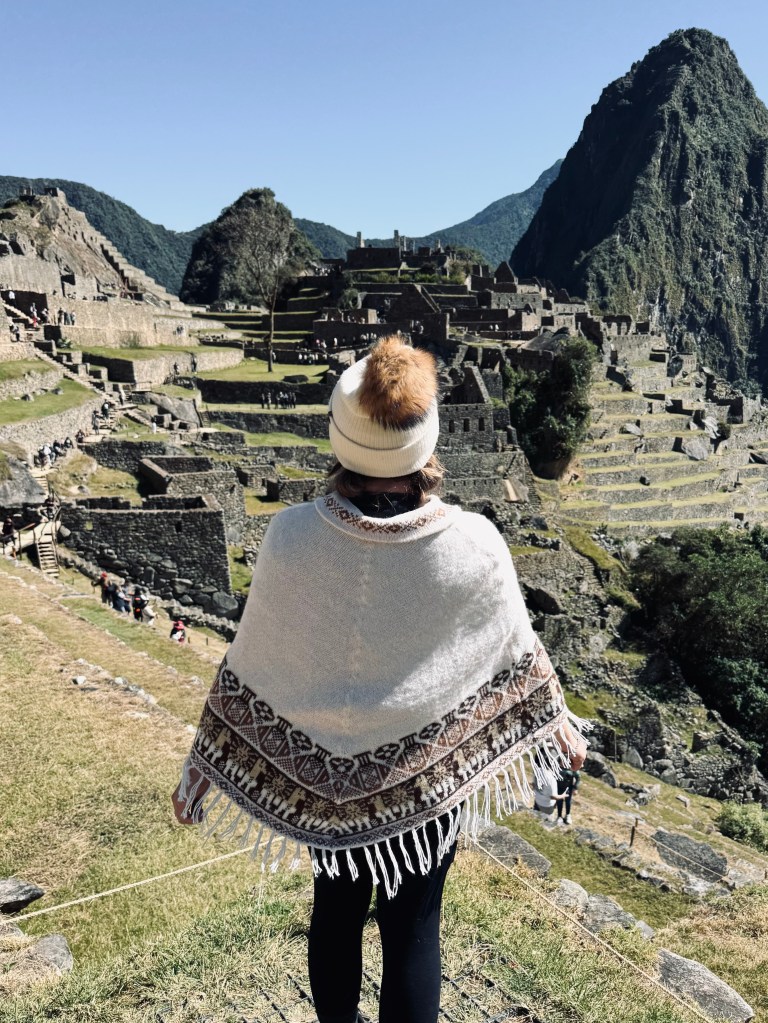 Girl wearing poncho and beanie looking out at Machu Picchu city ruins on the Inca Trail in Peru