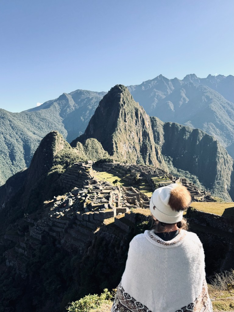 Girl wearing poncho looking out at iconic Machu Picchu view on the Inca Trail in Peru