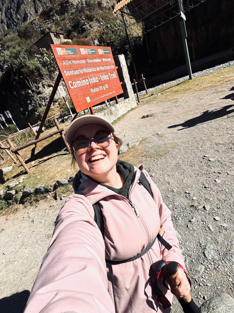 Girl in pink coat taking selfie at the starting point sign of the Inca Trail, Peru