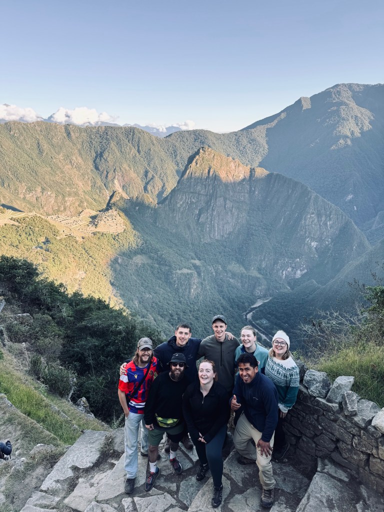 Trekking group standing together with view of Machu Picchu from the Sun Gate at sunrise on the Inca Trail in Peru