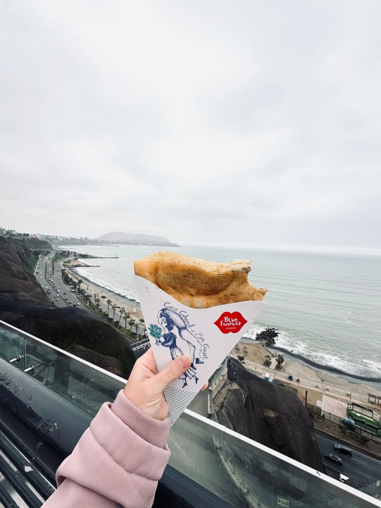Hand holding crepe with grey skies and ocean views in background in Miraflores, Lima, Peru