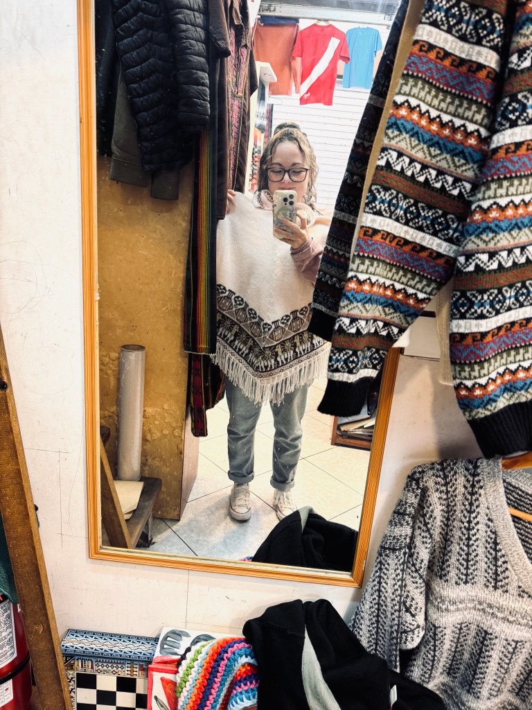 Girl trying on cream colored poncho at the Inka Markets in Miraflores, Lima, Peru