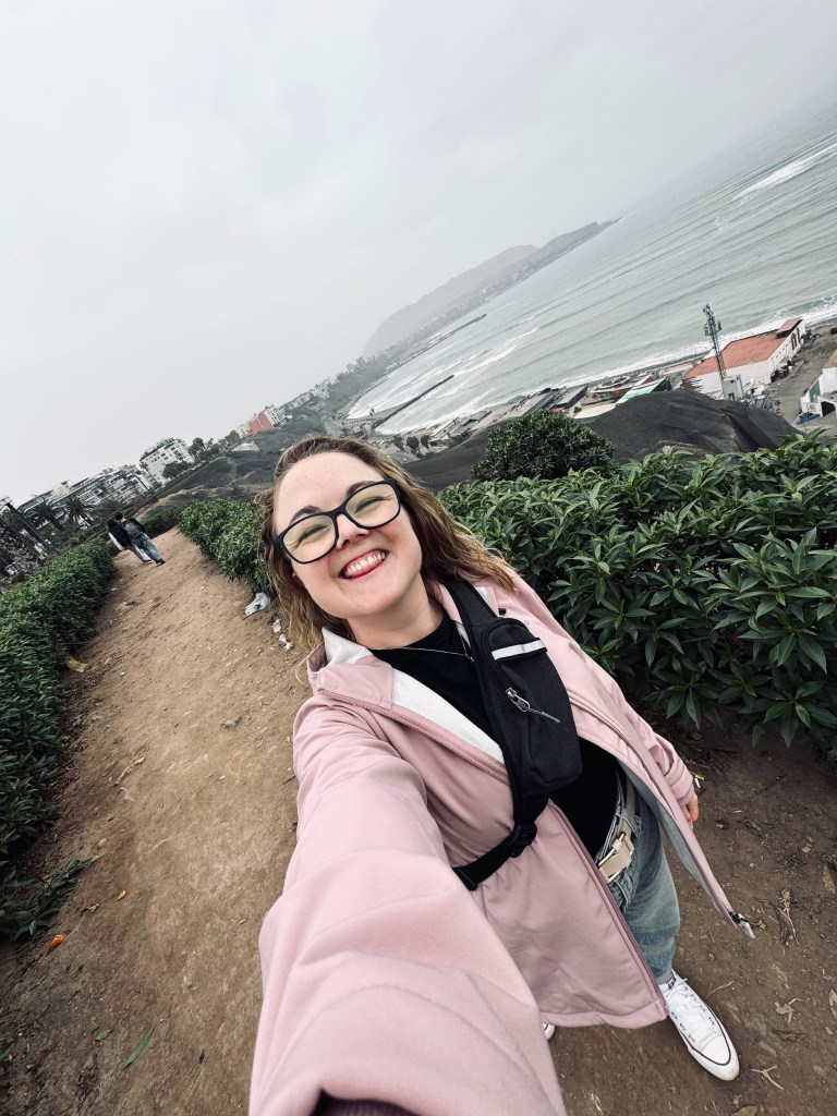 Girl smiling taking selfie with grey skies and ocean in background in Miraflores, Lima, Peru
