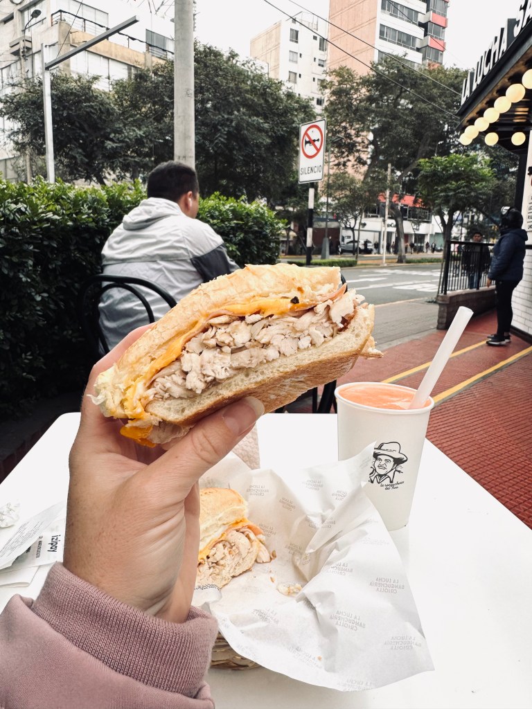 Hand holding chicken and cheese sandwich with street in background in Miraflores, Lima, Peru