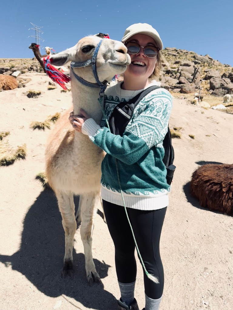 Girl in llama sweater smiling while hugging a llama in Peru