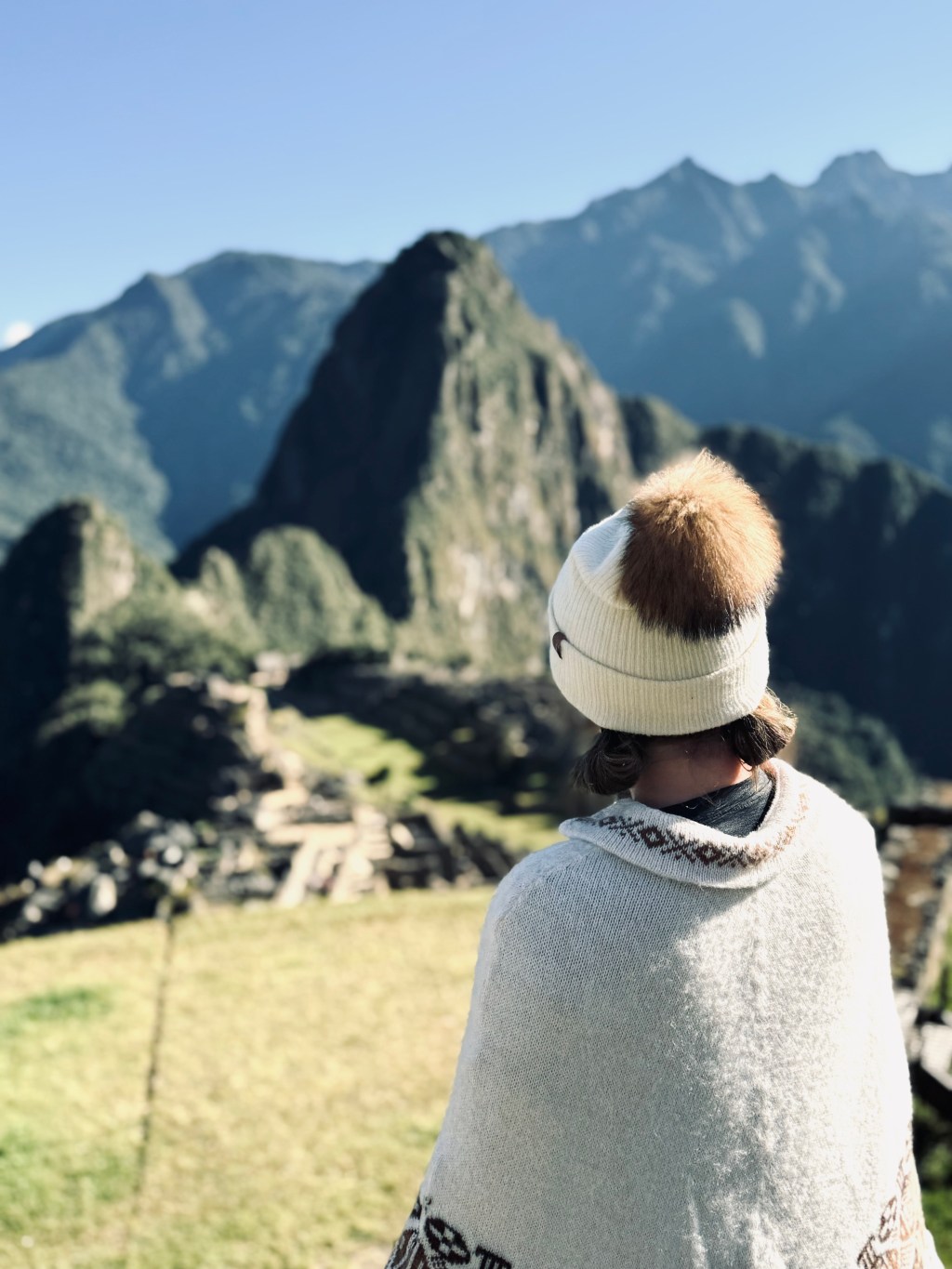 Girl in beanie and cream poncho looking out over Machu Picchu in Peru