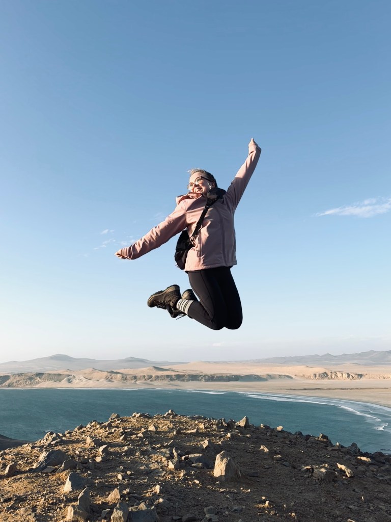 Girl jumping on a clear day with desert and ocean in the background in Paracas National Reserve, Peru