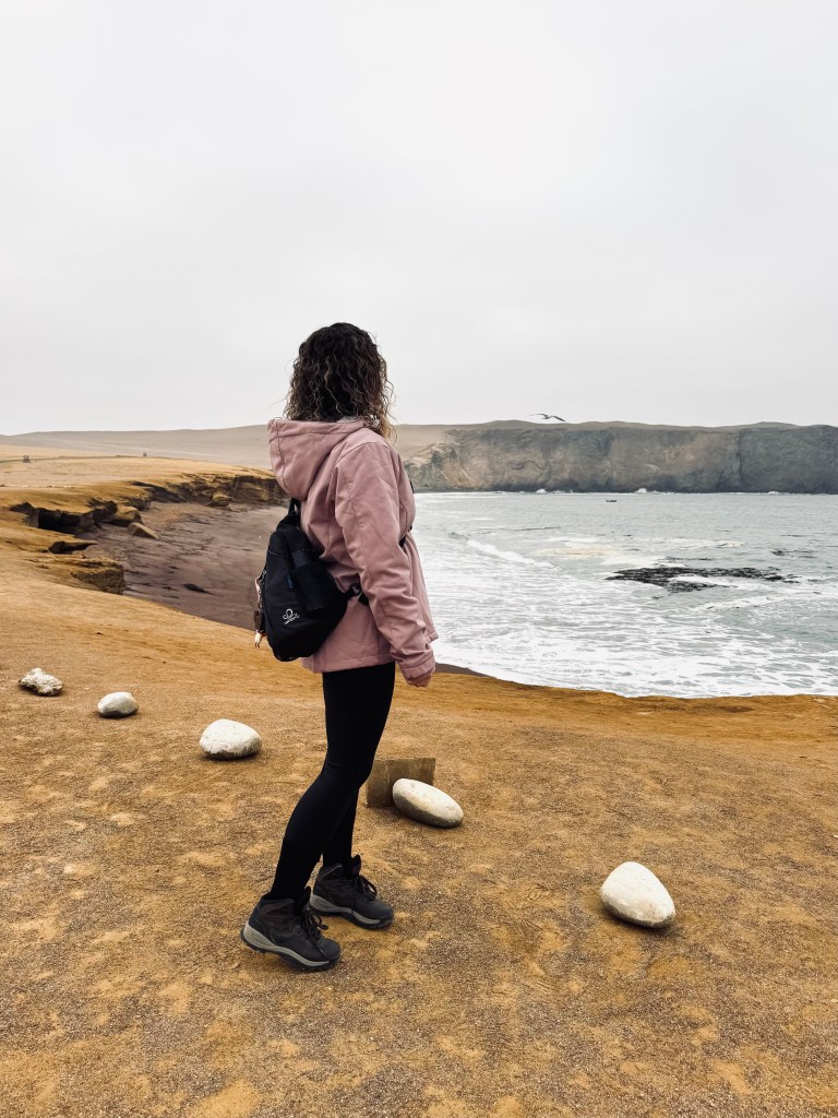 Girl looking out over desert and red sand beach in Paracas National Reserve, Peru