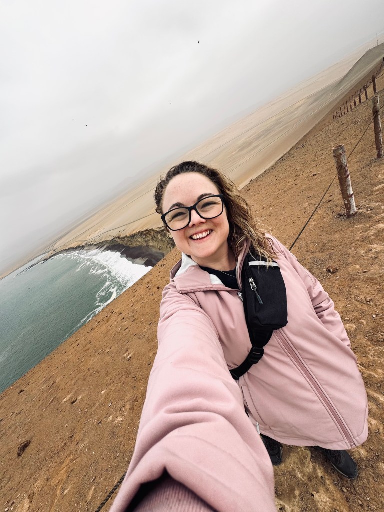 Girl taking selfie with cliffs, desert and ocean in background in Paracas National Reserve, Peru