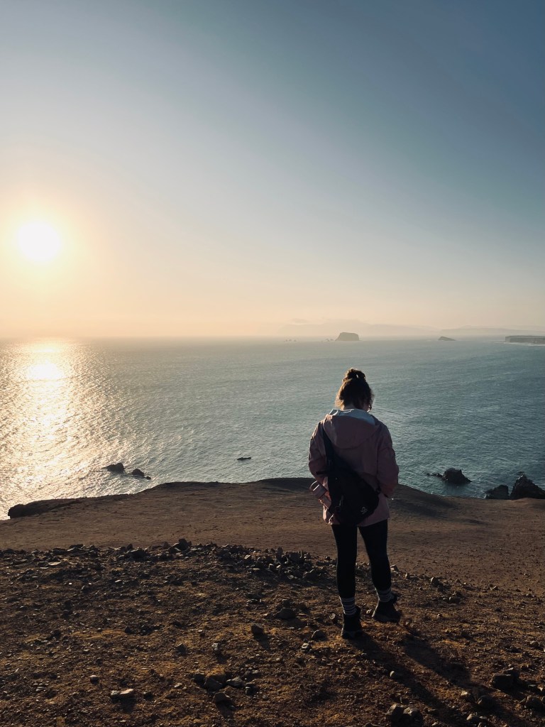 Girl looking out at sunset over ocean in Paracas National Reserve, Peru