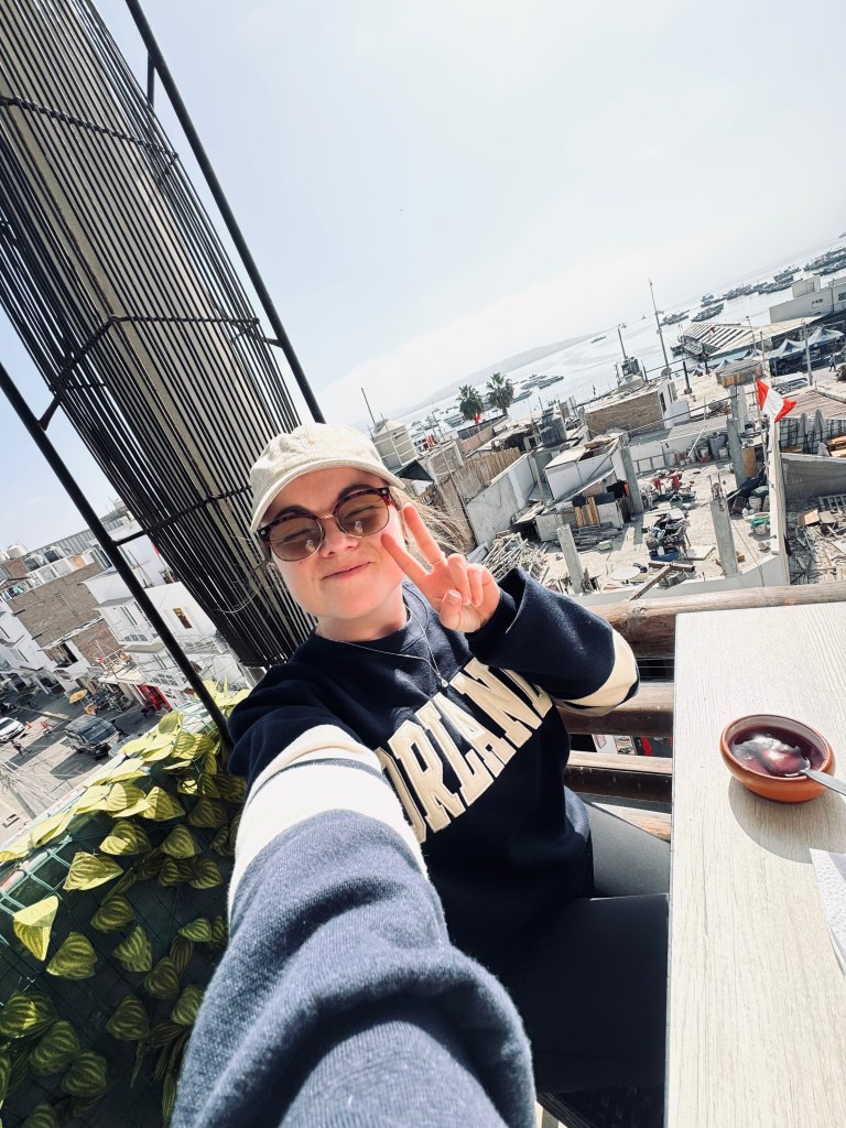 Girl taking selfie at a restaurant with town and ocean in background in Paracas, Peru