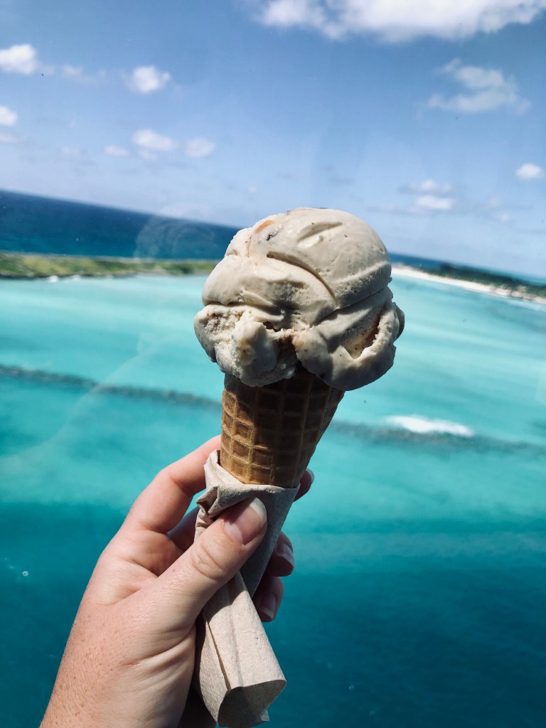 Hand holding an ice cream cone with blue carribean sea in background onboard a disney cruise ship