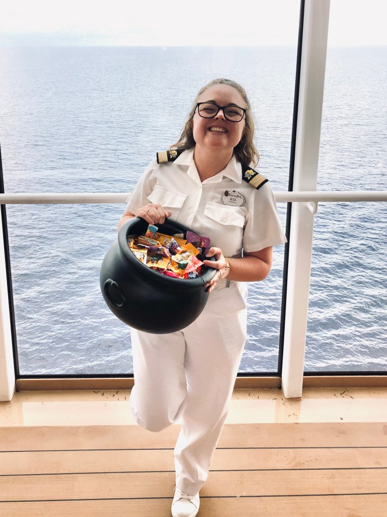 Disney officer in whites holding a trick or treat cauldron full of candy onboard a disney cruise ship