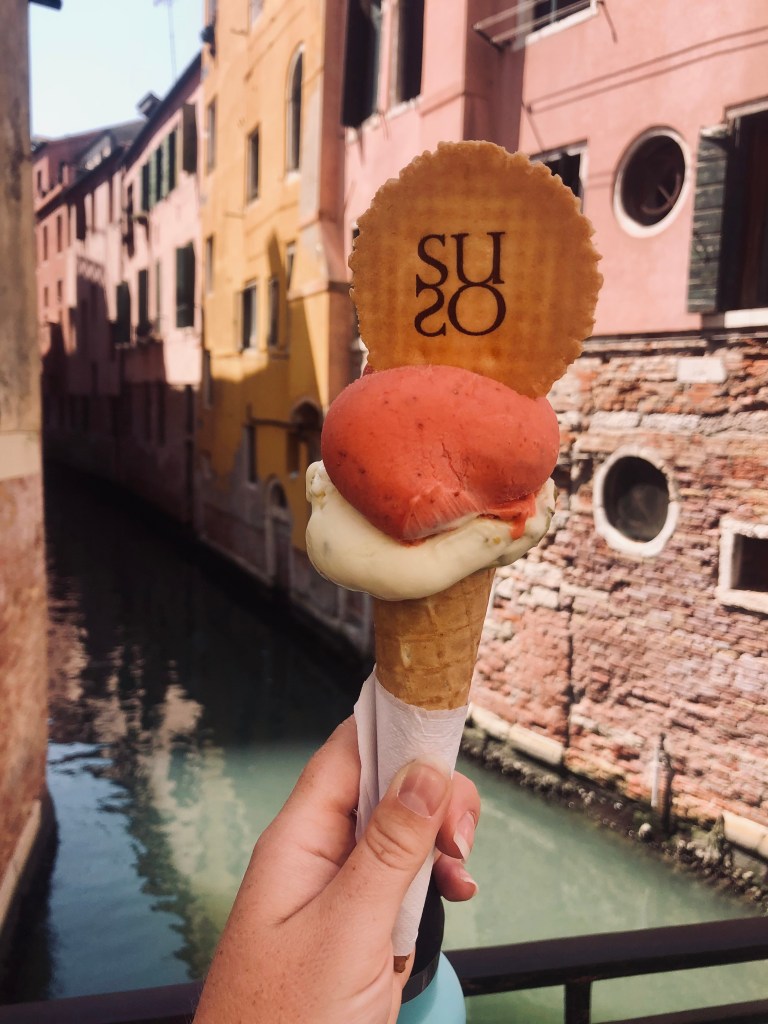 Hand holding gelato with canal in the background in Venice, Italy