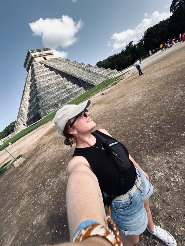 Girl taking selfie with pyramid in background at Chichen Itza, Mexico