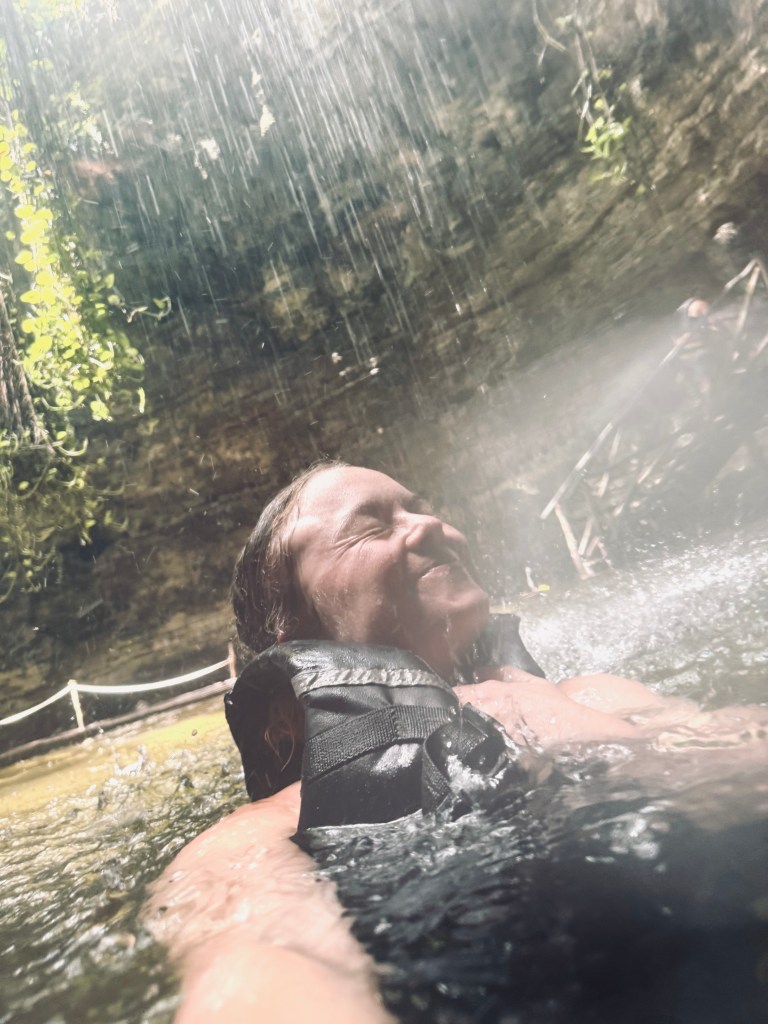 Girl in life jacket swimming under waterfall at Chichikan Cenote sinkhole in Mexico
