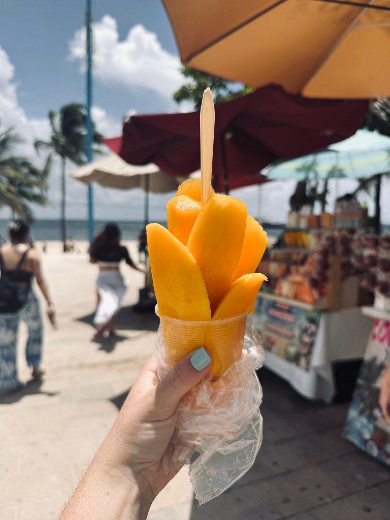 Hand holding cup of fresh mango on the beach at Playa del Carmen in Mexico