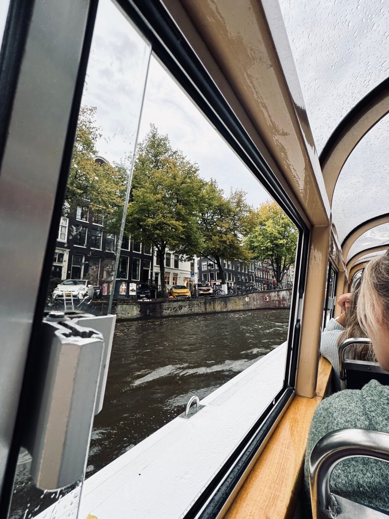 Window on a canal boat with canal and houses and trees in Amsterdam, The Netherlands