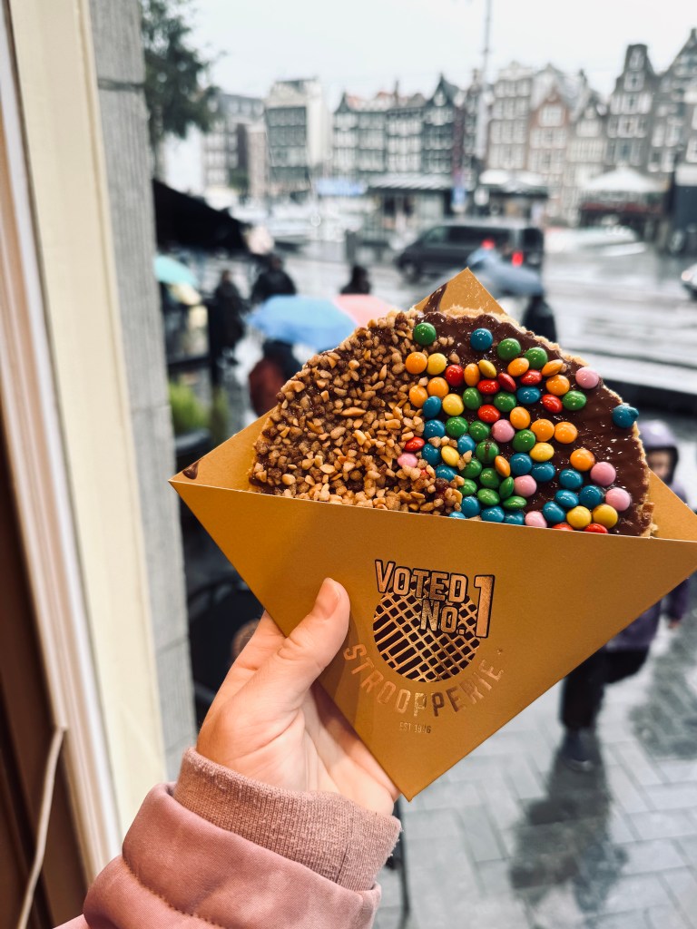 Hand holding a stroopwafel with m&ms and peanuts in gold packaging in Amsterdam, The Netherlands