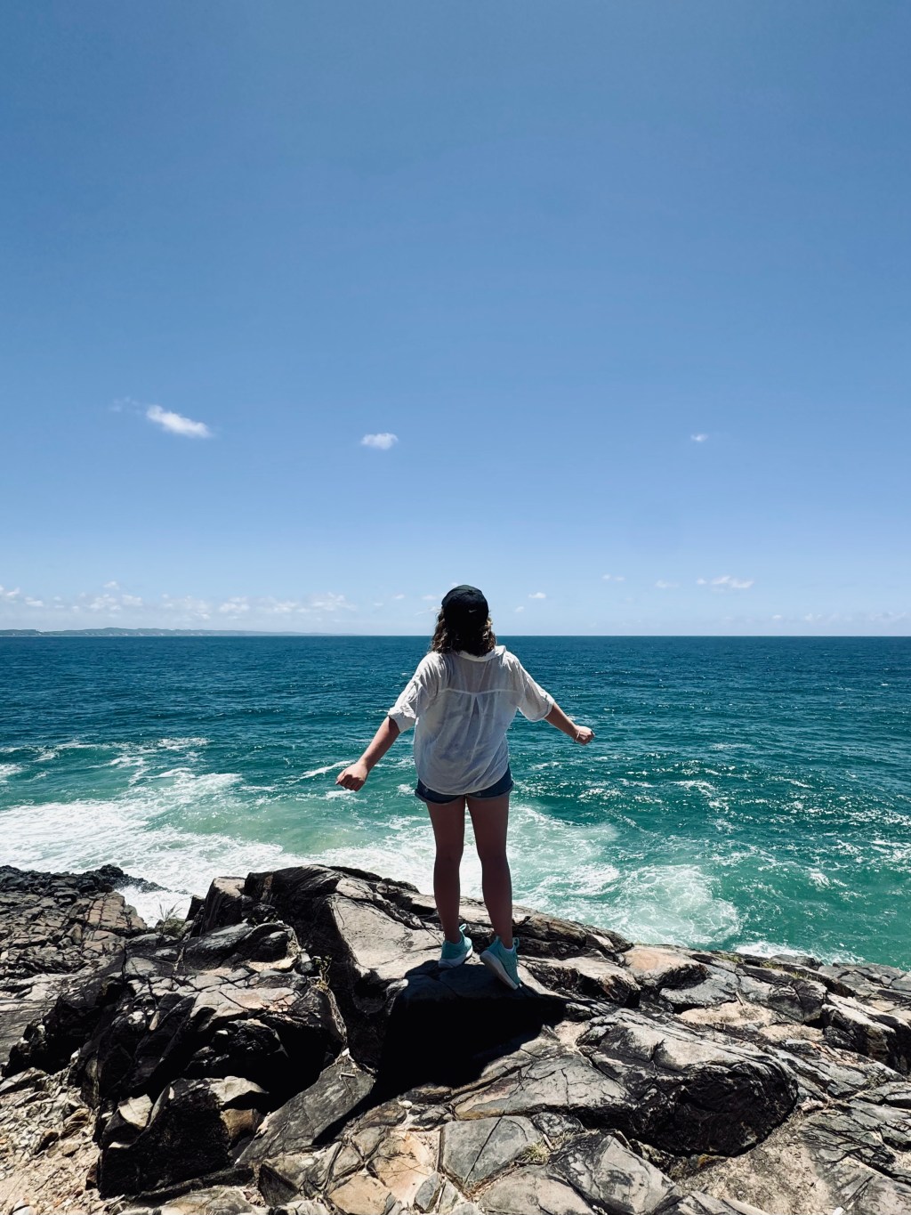 Girl looking out at blue ocean on a sunny day at Noosa National Park, Australia