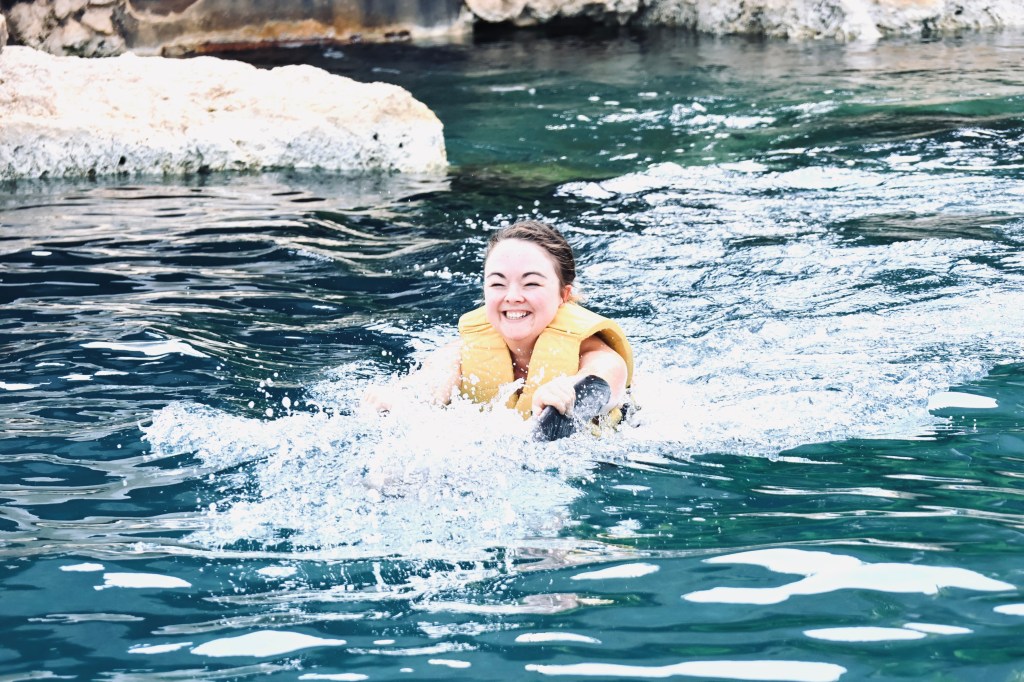 Girl in lifejacket smiling while swimming with dolphins